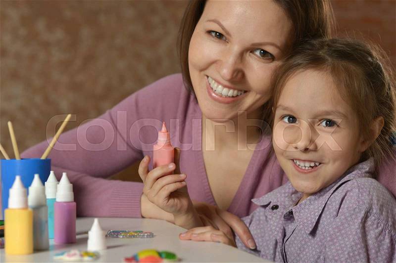 Portrait of a little girl painting with her mother, stock photo