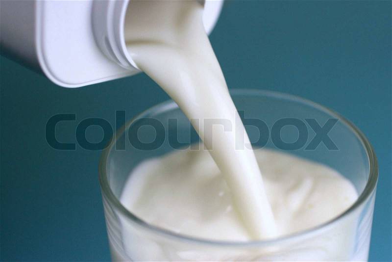 Pouring of milk from jug into a glass, stock photo
