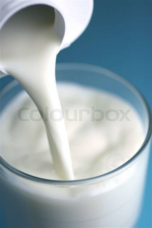 Pouring of milk from jug into a glass, stock photo
