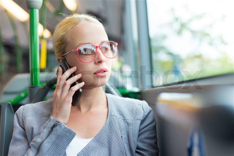 Blonde caucasian business woman talking on cell phone, traveling by bus. Public transport and commuting to work, stock photo