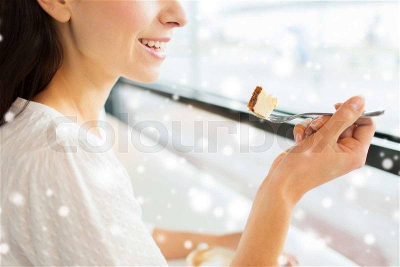 Food, dessert, people and lifestyle concept - close up of smiling young woman holding fork and eating cake at cafe or home over snow effect, stock photo