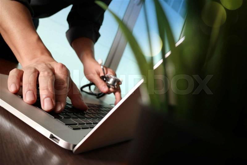 Doctor working at workspace with laptop computer in medical workspace office with green plant foreground, stock photo
