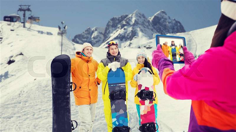 Winter sport, technology, leisure, friendship and people concept - happy friends with snowboards and tablet pc computer taking picture over snow and mountain background, stock photo
