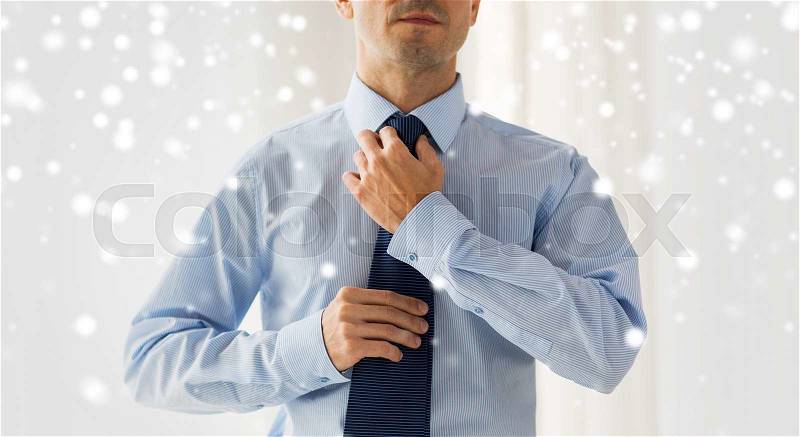 People, business, fashion and clothing concept - close up of man in shirt dressing up and adjusting tie on neck at home over snow effect, stock photo