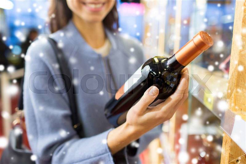 Sale, shopping, consumerism and people concept - happy young woman choosing and buying wine in market or liquor store over snow effect, stock photo