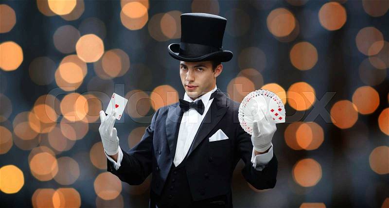 Magic, performance, gambling, casino, people and show concept - magician in top hat showing trick with playing cards over nigh lights background, stock photo