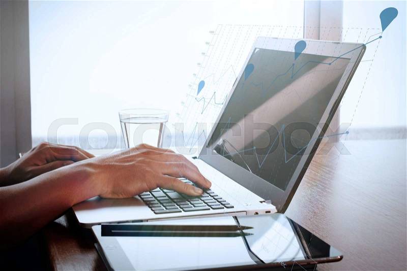 Designer hand working with digital tablet and laptop and notebook stack and eye glass on wooden desk in office with business graph diagram, stock photo