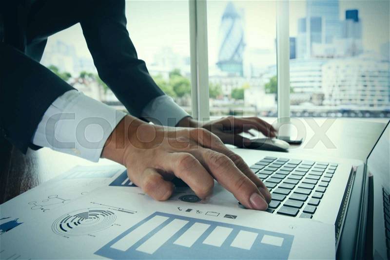 Close up of business man hand working on laptop computer on wooden desk as concept with social media diagram and london city blurred background , stock photo