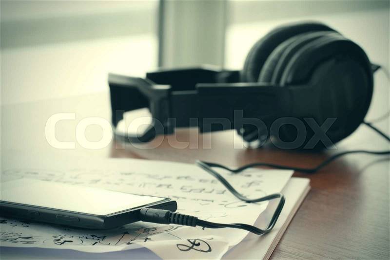 Closeup jack of smart phone with headphone on musical notes paper with shallow DOF evenly matched on wooden desk, stock photo