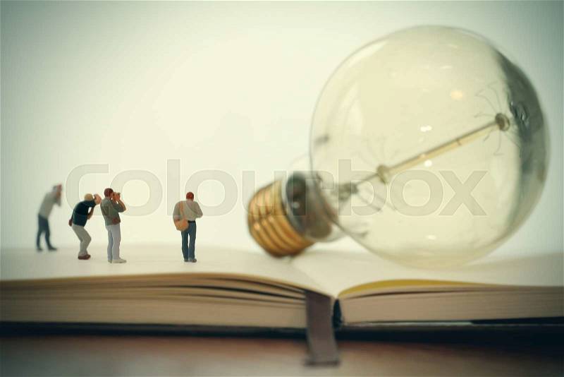 Creative idea concept - miniature photographer with vintage light bulb on open paper notebook, stock photo