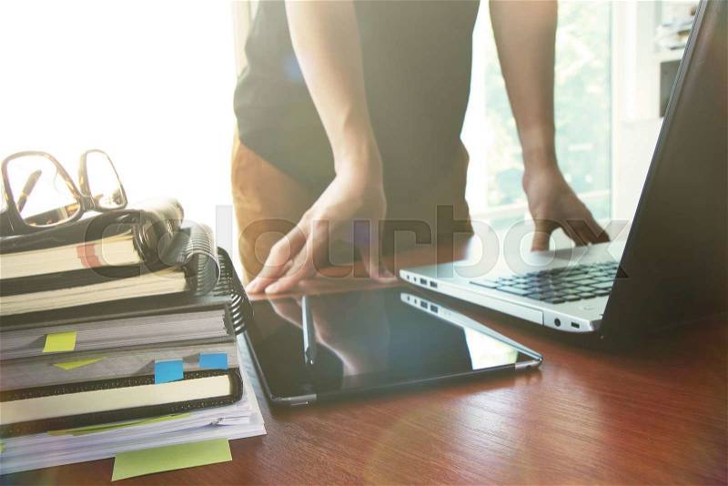 Designer hand working with digital tablet and laptop and notebook stack and eye glass on wooden desk in office, stock photo