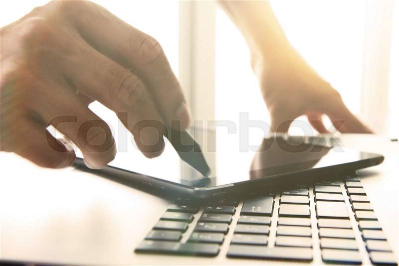 Designer hand working with stylus and digital tablet and laptop on wooden desk in office, stock photo