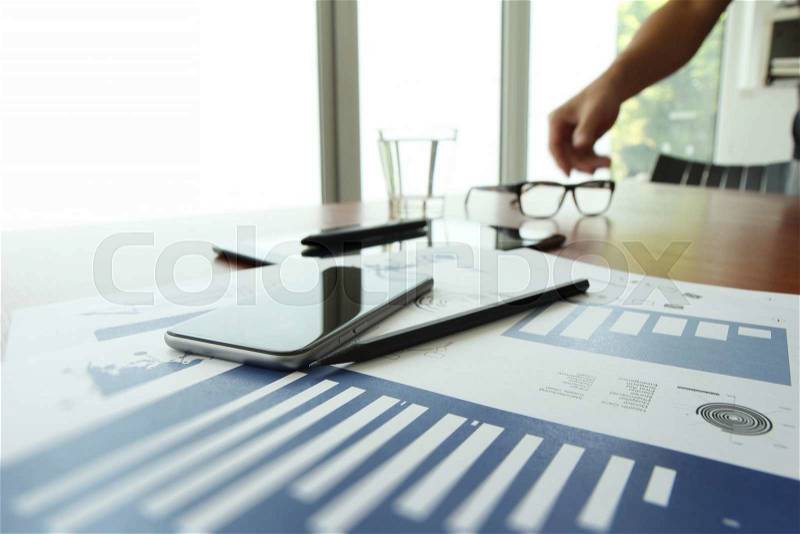 Business documents on office table with smart phone and digital tablet and man working in the background, stock photo