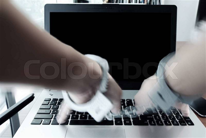 Businessman hand in handcuffs at wooden desk with laptop computer and digital tablet and stylus pen and smart phone as Cyber-Crime concept, stock photo