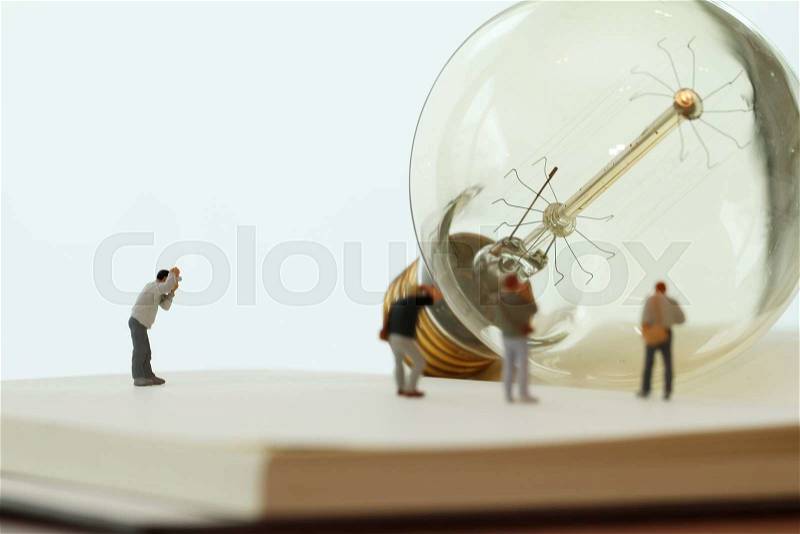 Creative idea concept - miniature photographer with vintage light bulb on open paper notebook, stock photo