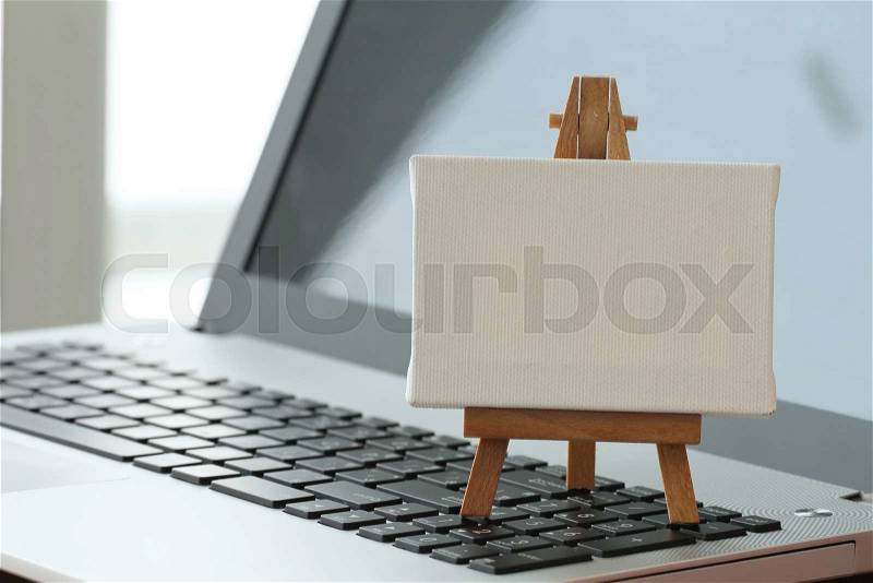Blank canvas and wooden easel on laptop computer as concept, stock photo