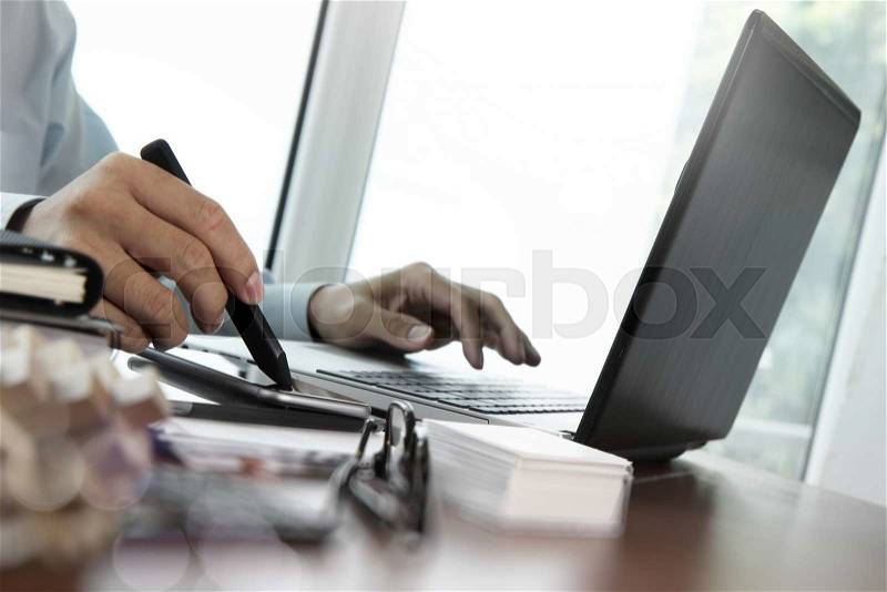 Designer hand working with stylus on smart phone and digital tablet and laptop on wooden desk in office, stock photo