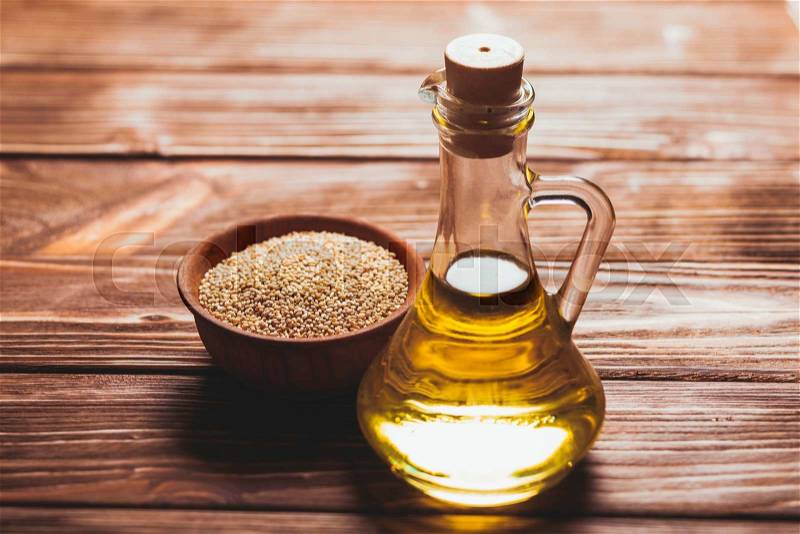 Sesame oil in a glass bottle with a cork and heap sesame seeds in a wooden bowl, stock photo