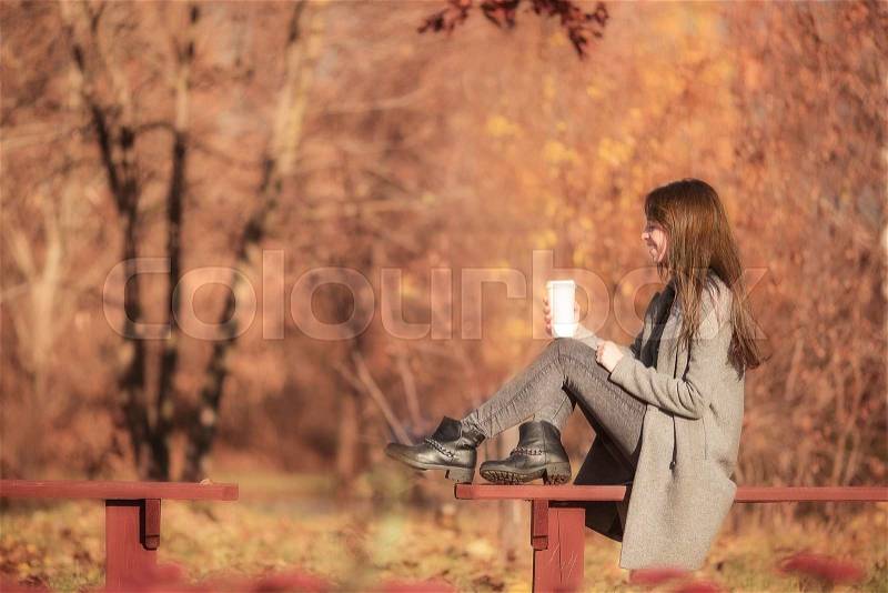 Fall concept - beautiful woman drinking coffee in autumn park under fall foliage, stock photo