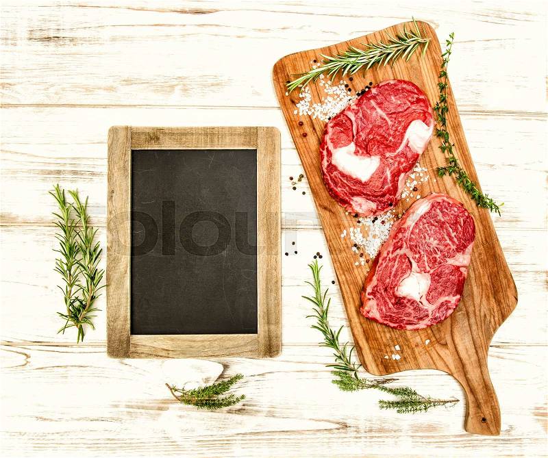 Raw fresh beef meat with herbs, spices and blackboard on wooden desk. Food background. Vintage style toned picture, stock photo