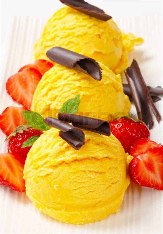 Three scoops of ice cream garnished with chocolate curls and strawberries, stock photo