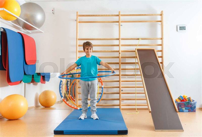 Young boy performs exercises with hula hoop in the gym, stock photo