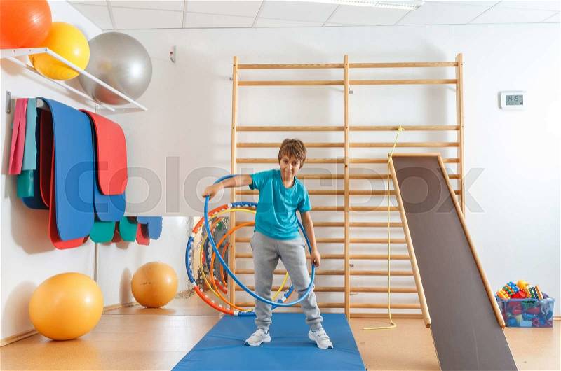 Young boy performs exercises with hula hoop in the gym, stock photo