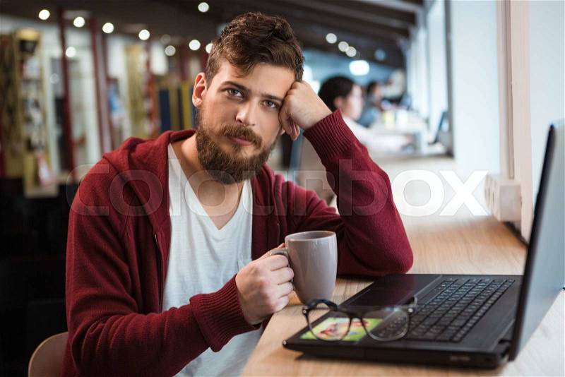 Handsome attractive young guy drinking coffe and using laptop siting in the office, stock photo