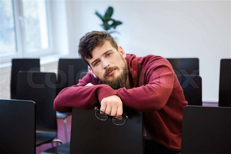 Handsome guy with beard looking exhausted sitting in meeting room, stock photo