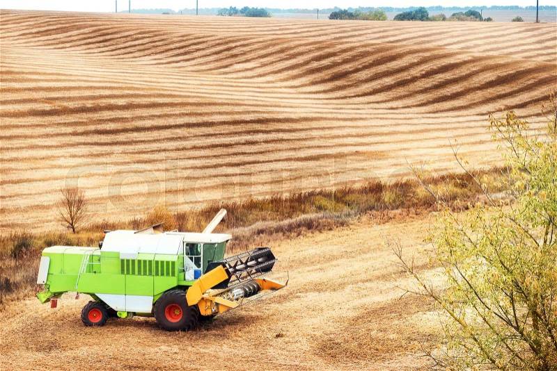 Wavy sloping field with combine in the corner, stock photo