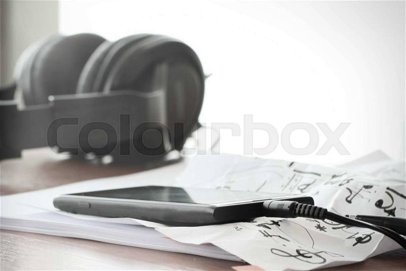 Closeup of smartphone with headphone on musical notes paper on wooden desk with shallow DOF evenly matched, stock photo