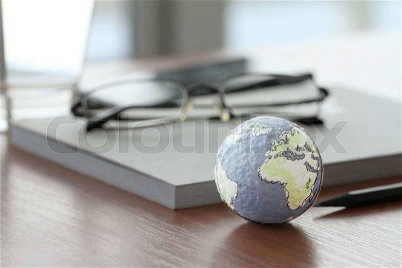 Hand drawn texture globe on wood table near note book and glasses, stock photo