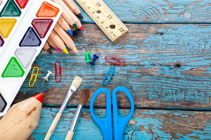 Pencils, scissors, paper clips and watercolor paints. Office or school supplies on wooden planks painted in blue, stock photo