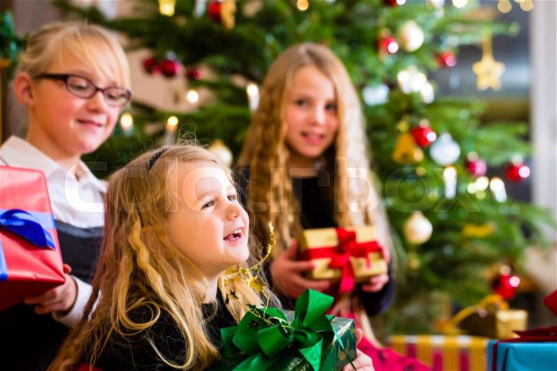 Children with Christmas gift on Christmas day in family home under tree, stock photo