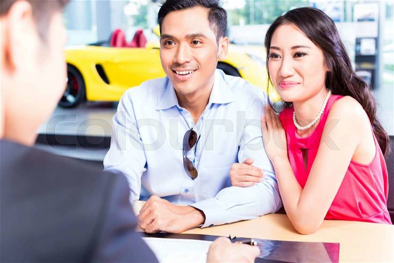 Asian Couple signing sales contract for car at dealership, stock photo