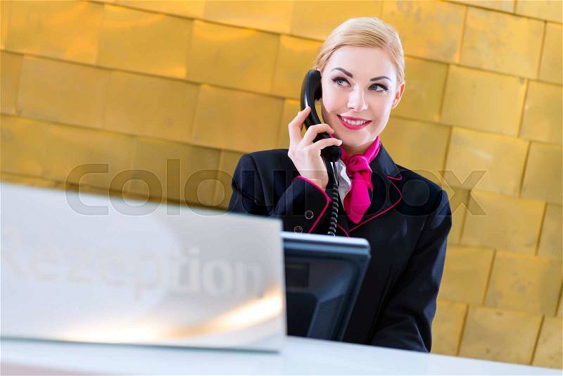 Hotel receptionist with phone on front desk, stock photo