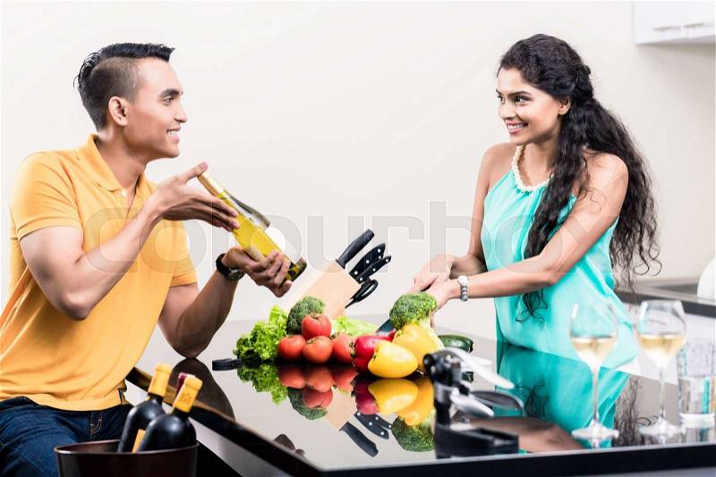 Indian woman and man in kitchen with red wine making salad, stock photo