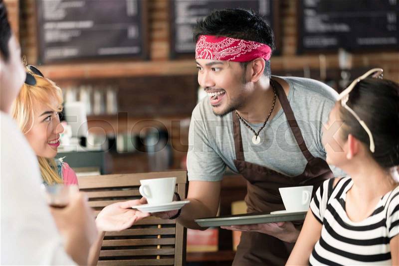 Waiter serving coffee in Asian cafe to women and man offering the drinks on a tray, stock photo