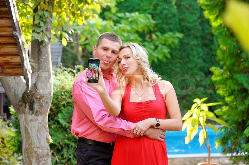 Couple fun taking self-portrait picture photos with mobile smart phone or pocket camera outdoors. Happy multiracial young couple in love taking pictures together on summer vacation. Man and woman, stock photo