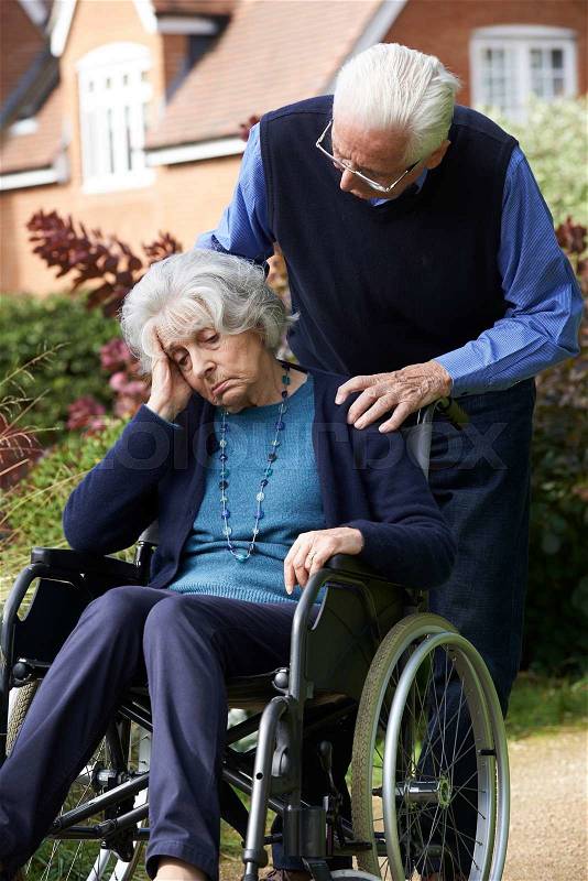 Depressed Senior Woman In Wheelchair Being Pushed By Husband, stock photo