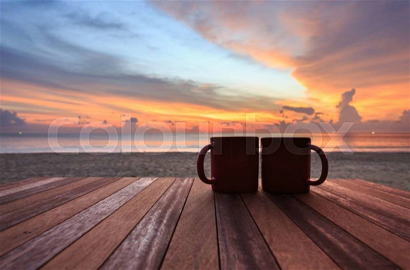 Close up coffee cup on wood table at sunset or sunrise beach, stock photo