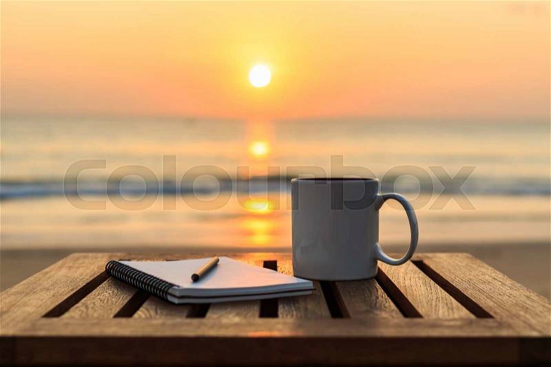 Close up coffee cup on wood table at sunset or sunrise beach, stock photo