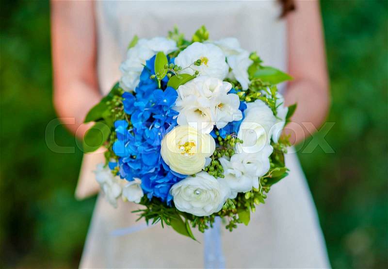 Bridal bouquet blue with white flowers in the bride\'s hands, stock photo