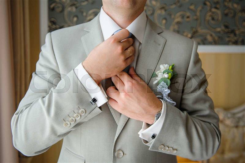 Man in a suit straightens his tie with cufflinks on their sleeves, stock photo