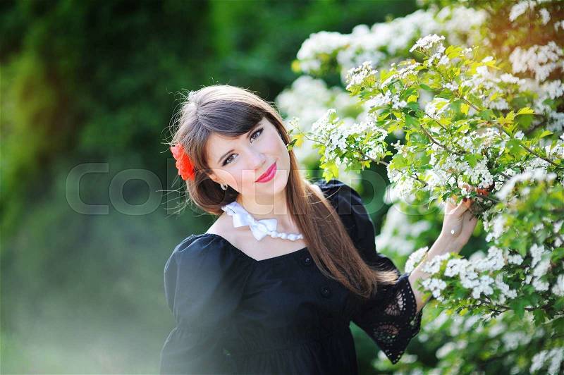 Beautiful girl with a red bow in the spring flowery park, stock photo