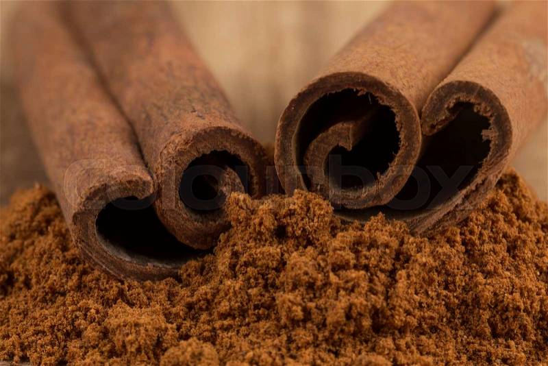 Cinnamon sticks with cinnamon powder on wooden background, stock photo