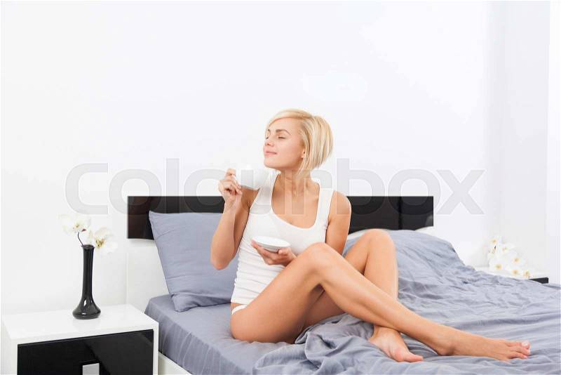 Woman hold cup of coffee smell closed eyes dream on bed, young blond girl happy smile morning bedroom home, stock photo