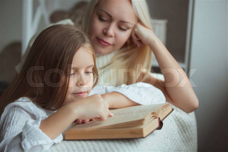 Mother with daughter reading book at home, stock photo