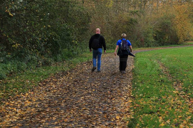 Couple, man and wife walk through the fallen leaves on the foot path in the park at the country side in autumn, stock photo