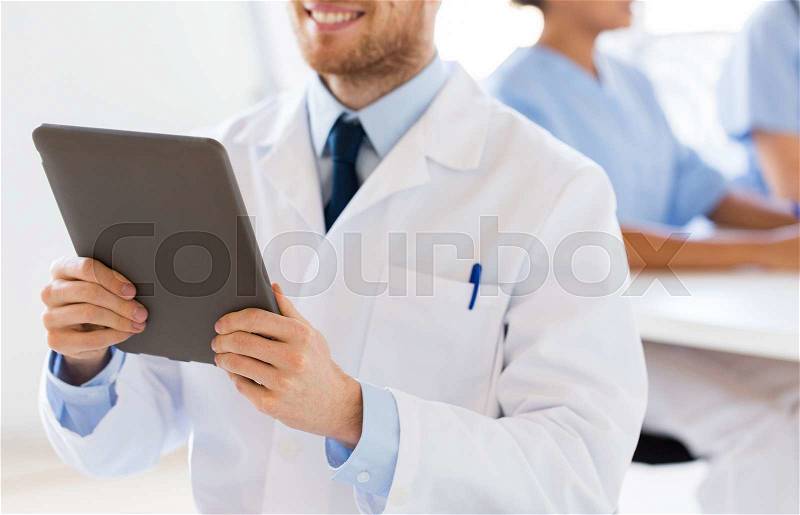 Technology, people and medicine concept - close up of happy male doctor with tablet pc computer over group of medics meeting at hospital, stock photo